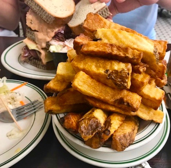 A huge pile of thick cut fries in a white bowl on a white plate both with thin green stripes on rim