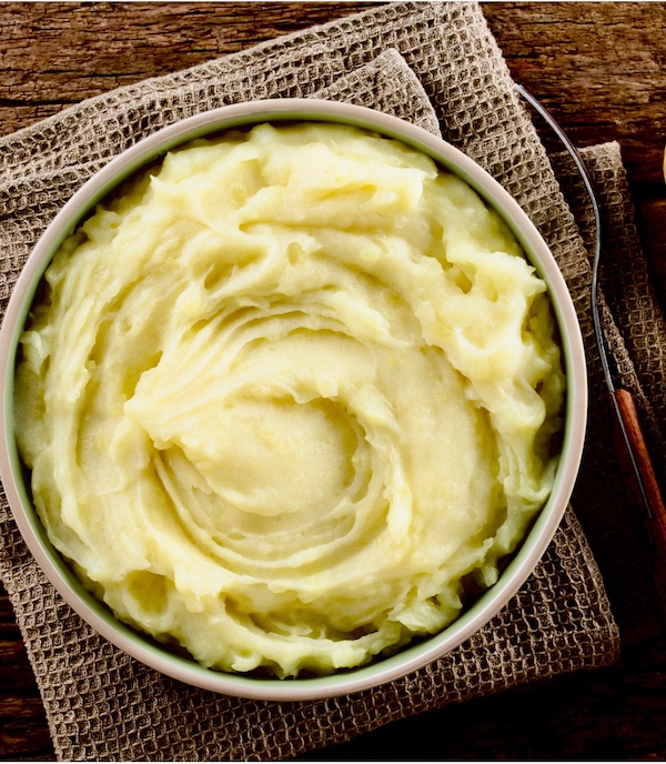 Large bowl of creamy Garlic Horseradish Mashed Potatoes sitting on a brown towel.