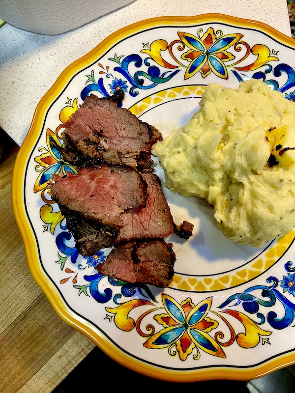 Garlic Horseradish Mashed Potatoes topped with a pat of melting butter sit next to sliced steak on a plate with a yellow and blue rim.