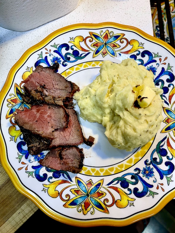 Garlic Horseradish Mashed Potatoes topped with a pat of melting butter sit next to sliced steak on a plate with a yellow and blue rim.