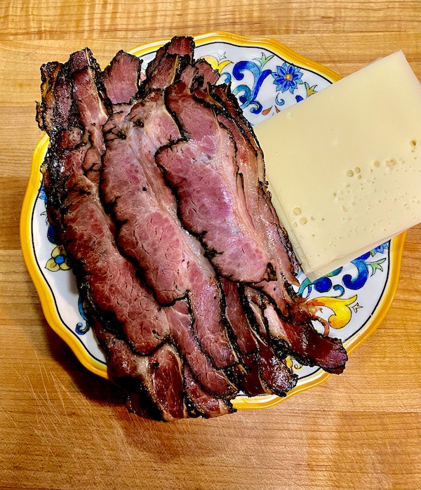 Wood counter with plate of sliced pastrami and slices of Swiss cheese from Canter's Deli on Fairfax