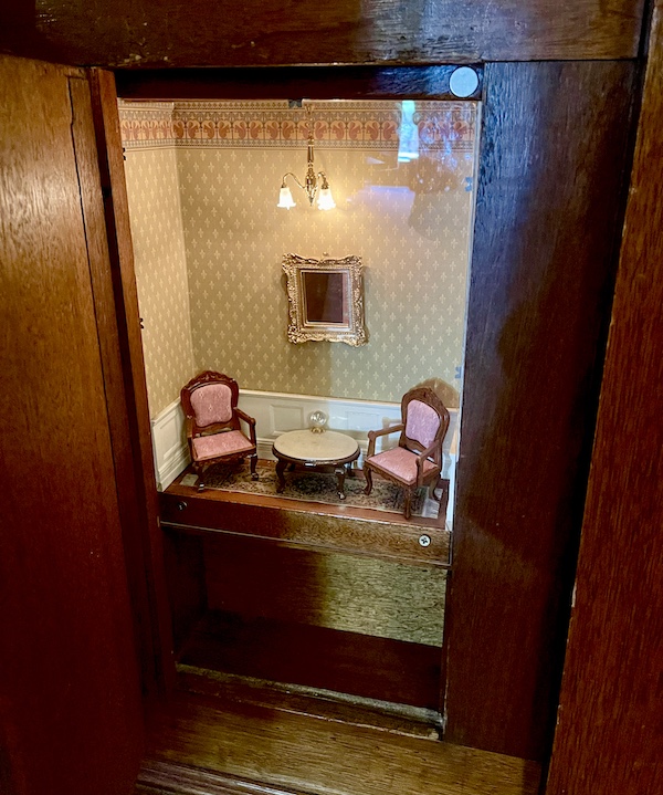 Wood and glass case displaying Victorian miniature chairs and table in the hotel lobby.