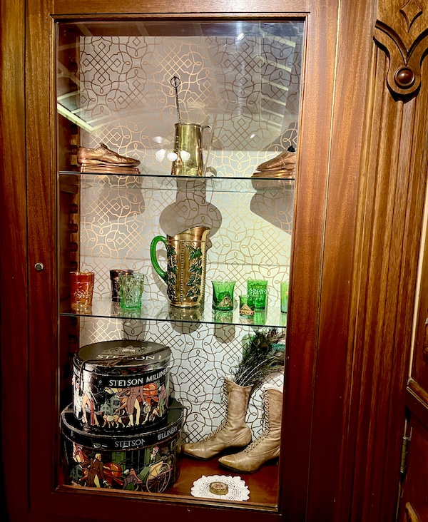 Glass case with green glass shot glasses, pitcher and high button shoes at the Strater Hotel Durango Colorado