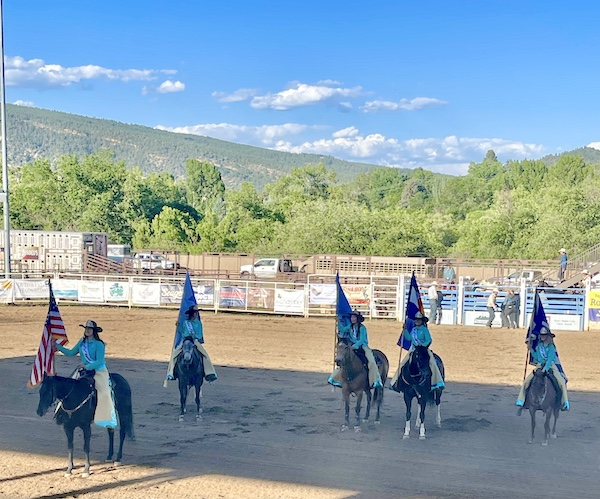 Five horses with female riders holding 5 different flags at Our First Rodeo Durango CO