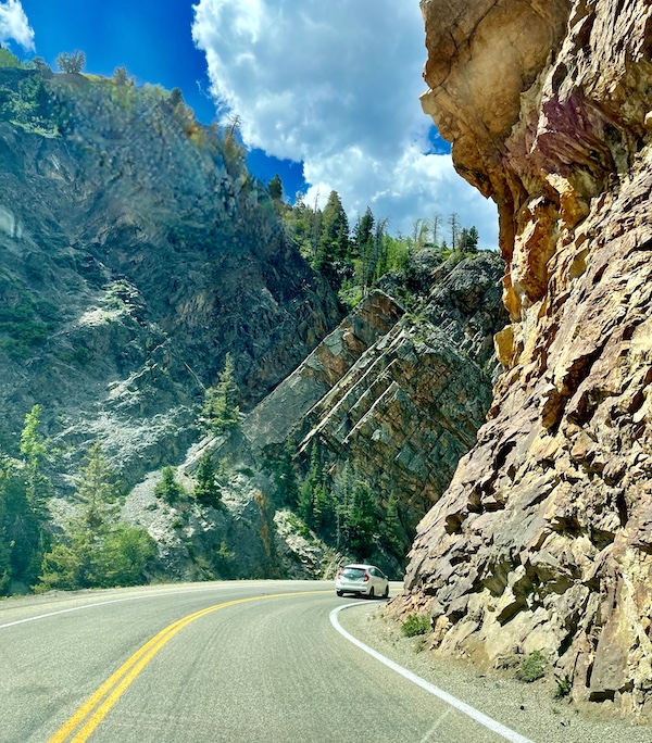 Angular gray peaks on left of highway and craggy tan rock on right.