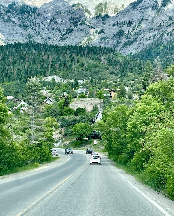 Highway leading into Ouray with some homes visible through the trees in the distance.